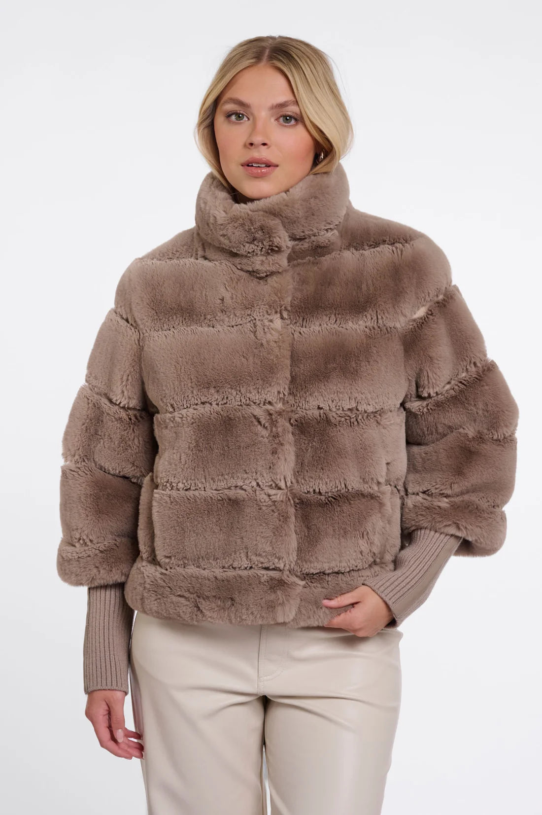 Model wearing a taupe faux fur jacket with ribbed knit sleeves, a stand-up collar, and a relaxed silhouette.
