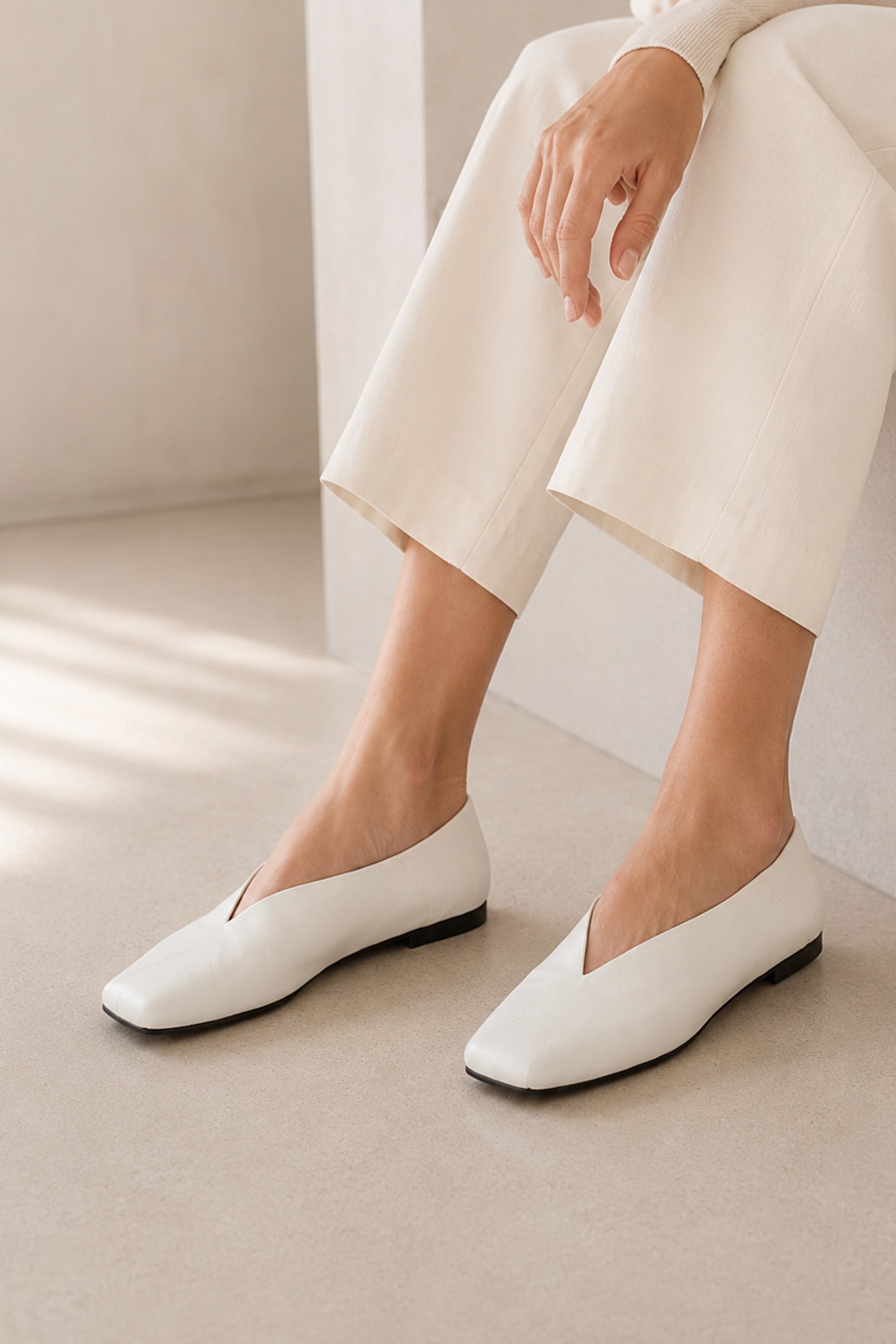 Ivory square-toe flat shoes with a deep V-cut design, styled with cropped cream pants in a minimalist fashion look