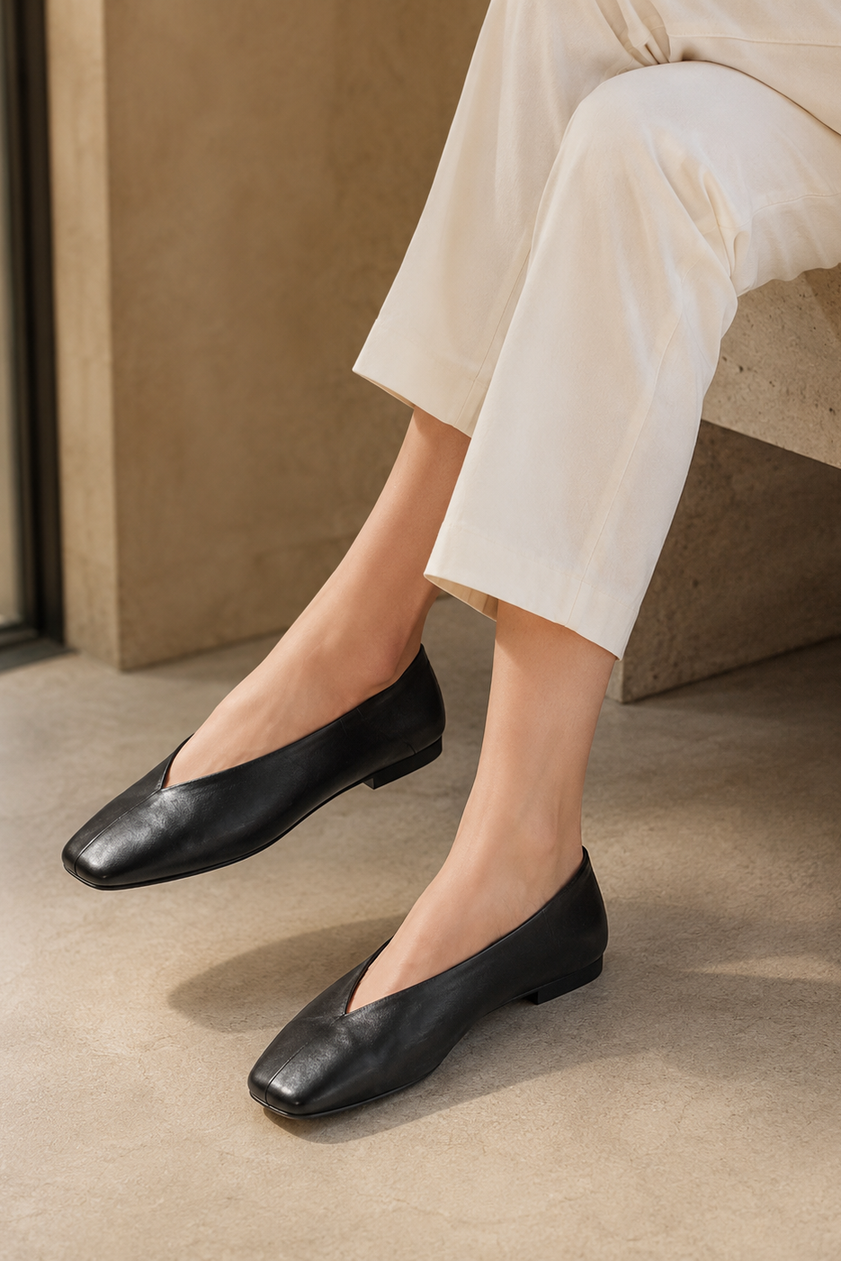 Black square-toe flat shoes with a deep V-cut design, styled with cropped cream pants in a modern minimalist fashion look